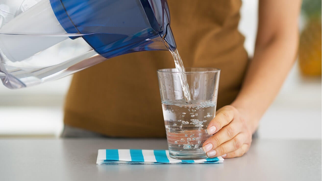 Frau gießt sich ein Glas Wasser ein, um Mundtrockenheit zu vermeiden